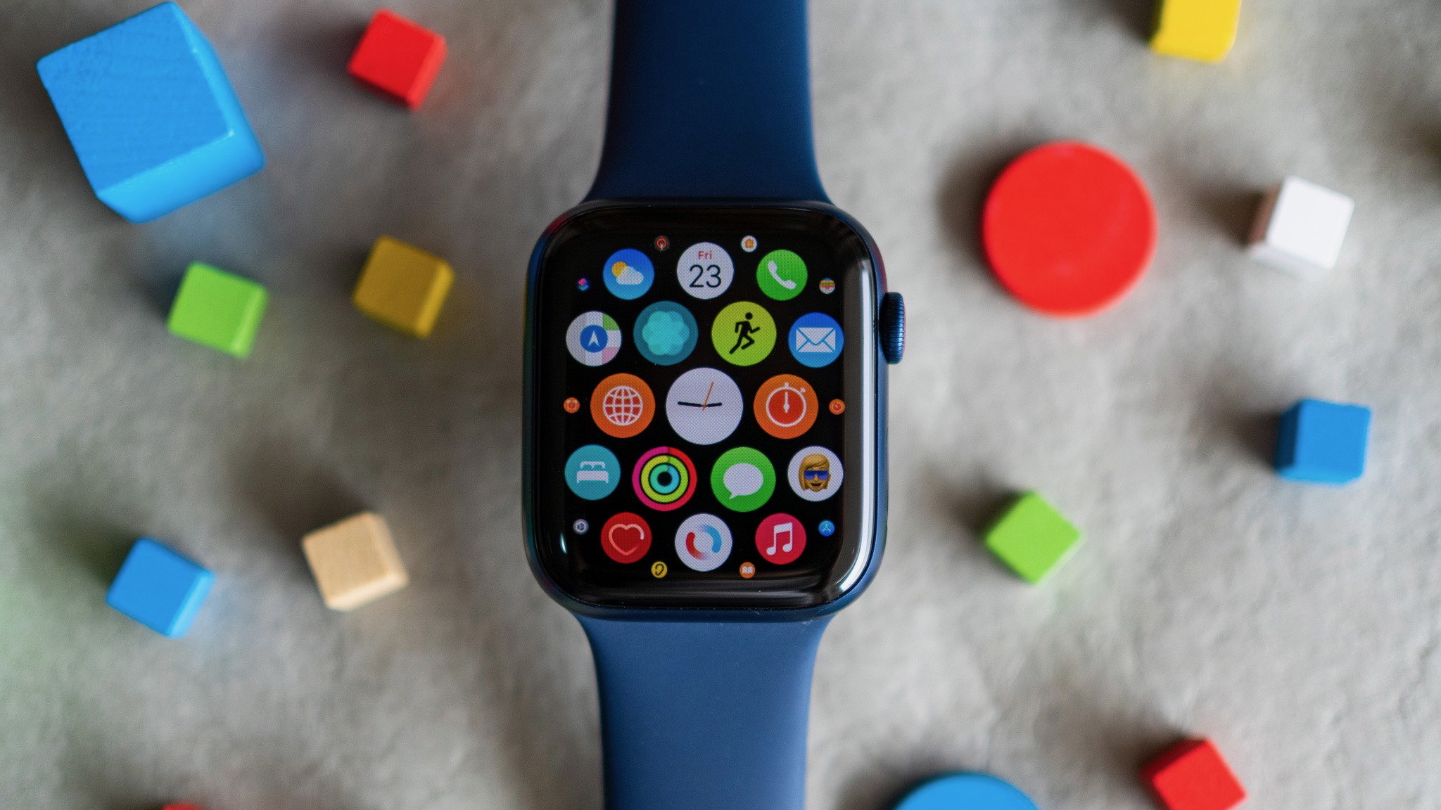 Apple Watch Series 6, що сидить над фетровою підлогою з барвистими блоками, що оточують його, на дисплеї, що показує колекцію піктограм додатків.