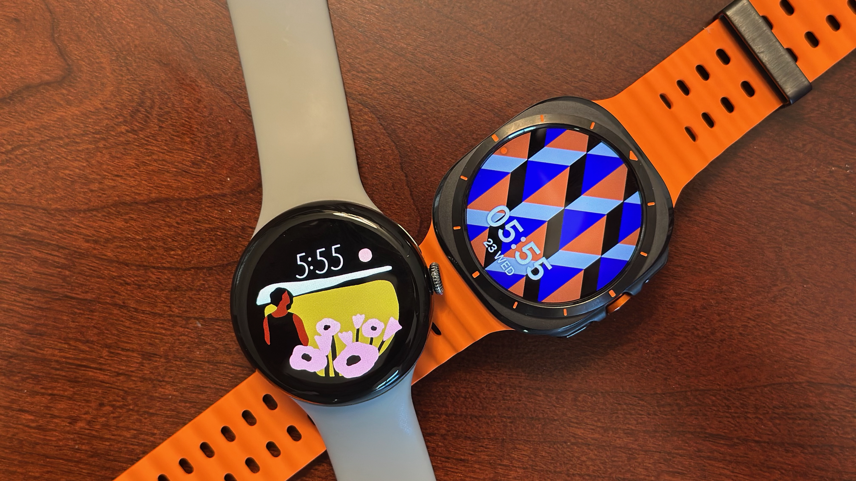 Google Pixel Watch 3 сидить біля Samsung Galaxy Watch Ultra на коричневому столі, обидва з барвистими годинниками.