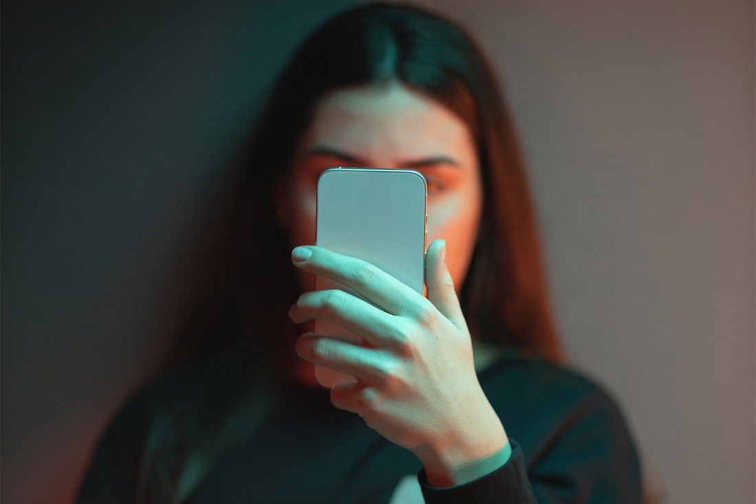 Людина, що тримає смартфон із синім екраном світла, що висвітлює обличчя в тьмяно освітленій кімнаті.