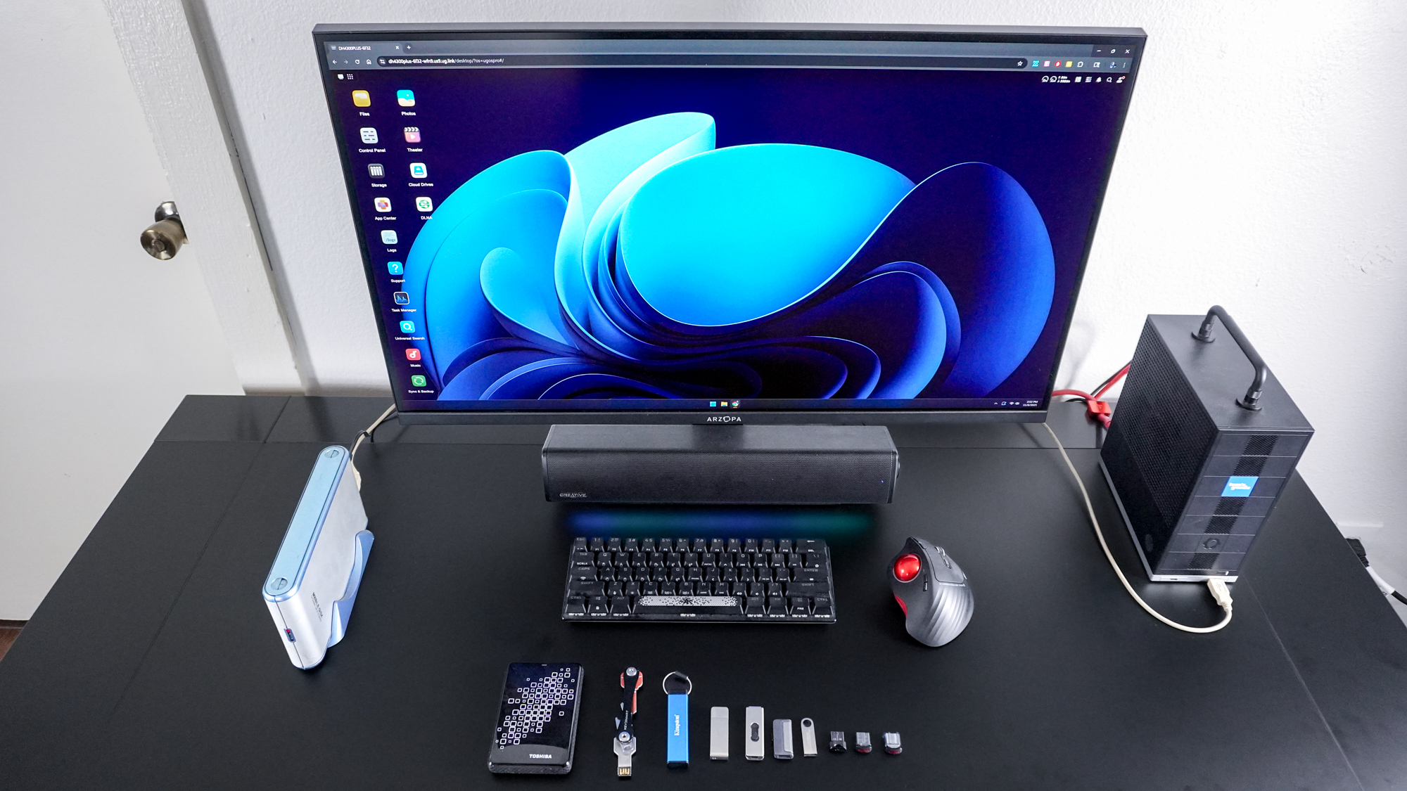 Знімок зверху, на якому показано комп’ютер, підключений до Ugreen NASync DH4300 Plus у веб-браузері, з флеш-накопичувачами та зовнішніми жорсткими дисками на столі